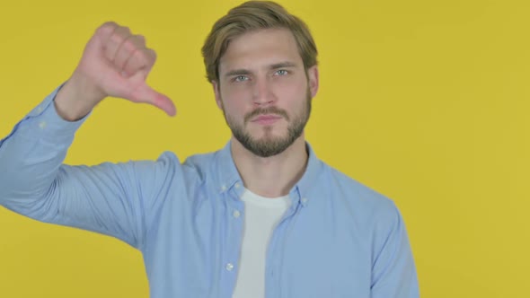 Thumbs Down By Young Man on Yellow Background