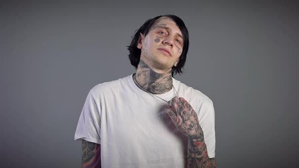 Front View of Confident Young Tattooed Man Stretching Neck and Hands Exercising at Grey Background