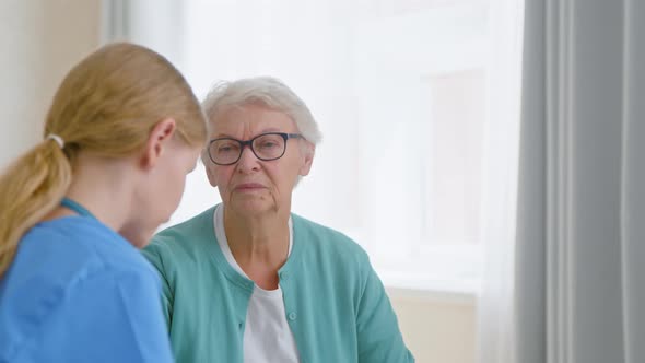 Senior lady patient with glasses talks to experienced young caretaker