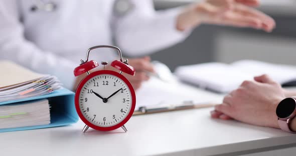 Red Alarm Clock Standing on Table of Doctor and Patient Closeup  Movie Slow Motion