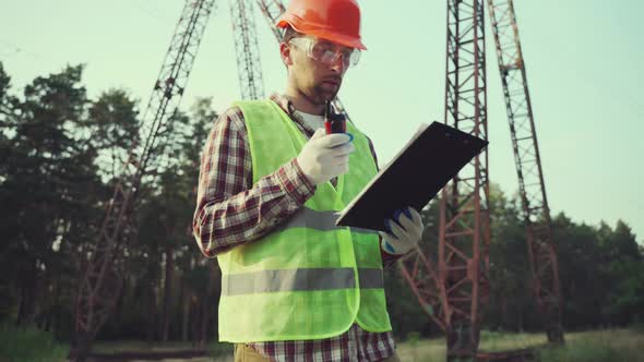 Electrical Engineer Wearing Hard Hat and Safety Vest Checking Electrical Systems on High Voltage