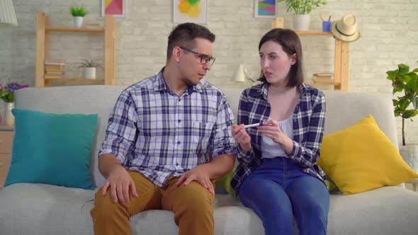 Young Disappointed Married Couple Sitting in Living Room Learns About Negative Pregnancy Test