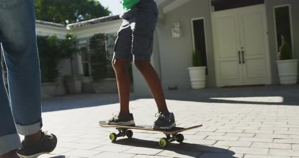 African american dad teaching his son to skateboard in the front yard
