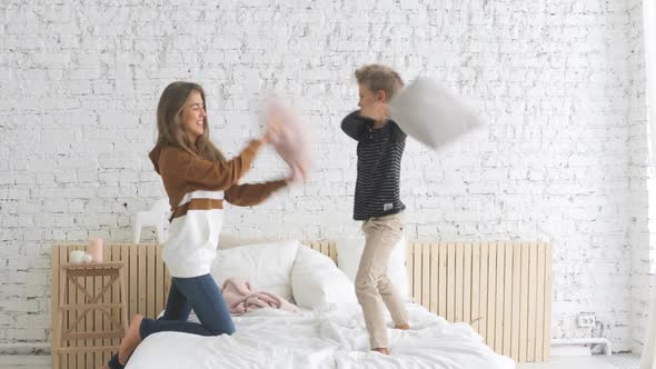 Happy Family Mother and Son Having Funny Pillow Fight on Bed in Nursery at Home