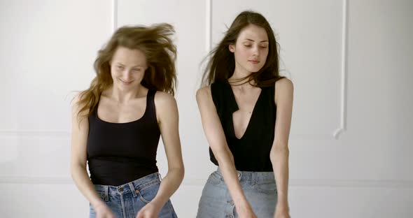 Two Young Carefree Girls Are Dancing Joyfully in Studio in White Background, Fan Is Blowing