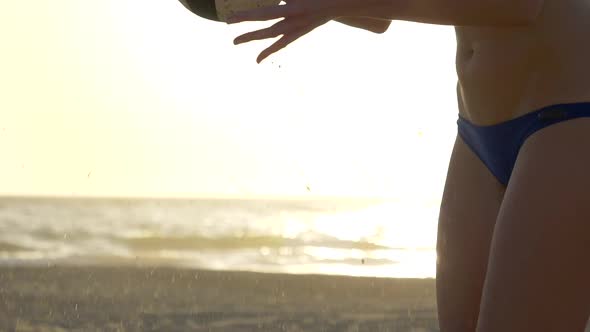 Women players play beach volleyball and a player serves the ball.