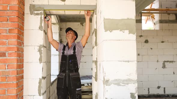 Construction worker at construction site measures the length of the window opening