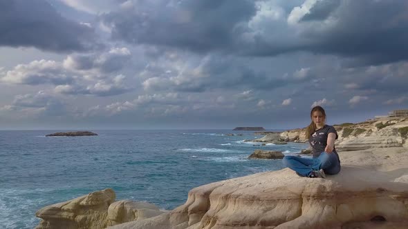 A Girl Sits on a Rock on the Sea Coast