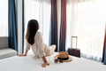 Young asian woman traveler with luggage sitting and relaxing on the bed in hotel room - PhotoDune Item for Sale
