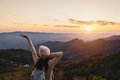 Happy young woman traveler relaxing and looking at the beautiful sunset on the top of mountain - PhotoDune Item for Sale