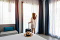 Young woman traveler with luggage looking at view in hotel room on summer vacation - PhotoDune Item for Sale