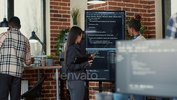 Software engineer holding digital tablet analyzing code on wall screen tv explaining errors to