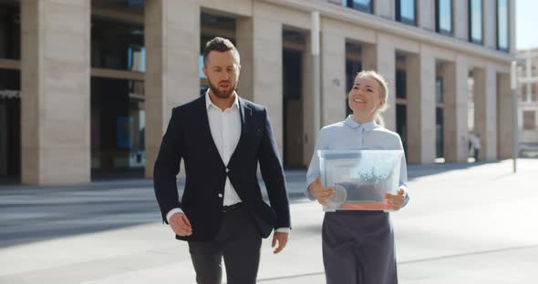 Smiling Businesswoman Carrying Box with Personal Stuff Talking with Colleague Walking Outdoors