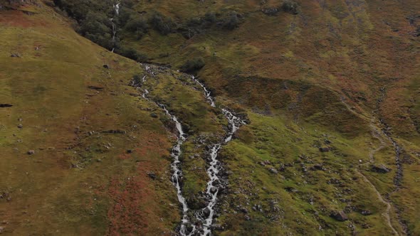 Aerial pullaway from a river rushing its way down a Scottish hillside in the highlands of Glencoe, S