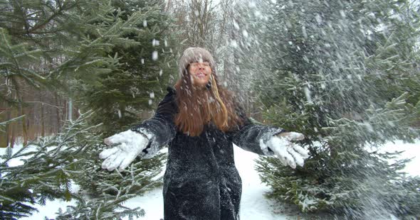 Playful Young Woman Throws Snow Up and Smiling in Front of the Tree in Forest