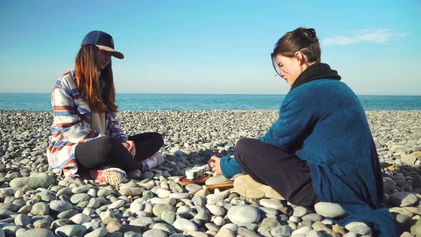 Two women are preparing for tea ceremony. sitting in lotus position on seashore.
