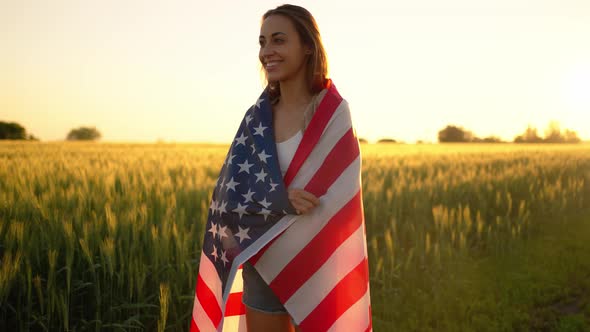 American Woman Covered with Flag of America at Sunset on Wheat Field