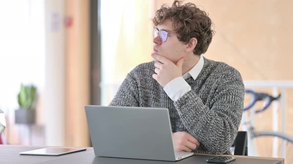 Pensive Young Man with Laptop Thinking at Work 