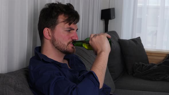 Desperate and drunk man drinking on the couch in his living room.