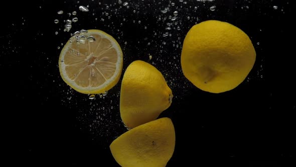 Slow Motion Lemon Halves Falling Into Transparent Water on Black Background