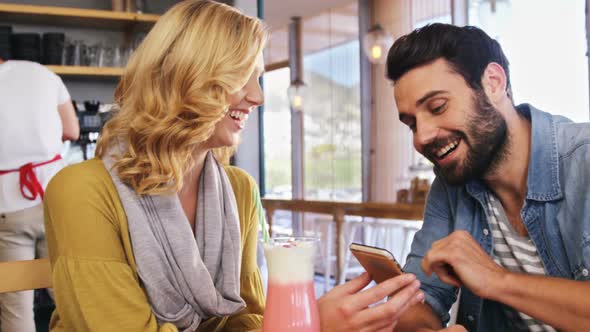 Couple using mobile phone while having a cup of coffee and milkshake