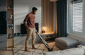 Young man hoovering carpet with vacuum cleaner in living room - PhotoDune Item for Sale