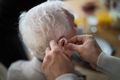 Close-up of caregiver man's hand inserting hearing aid in senior's man ear - PhotoDune Item for Sale