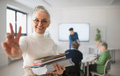 Happy senior woman student with books raising hand and looking at camera in classroom - PhotoDune Item for Sale
