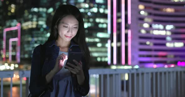 Woman sending sms on cellphone in city at night 