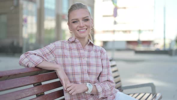 Young Woman Smiling at Camera While Sitting on Bench