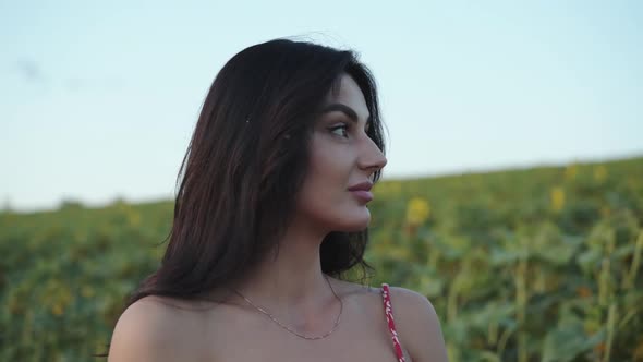 Beautiful Girl Looks with Light Smile Tucks Hair By the Earsand Among Sunflowers