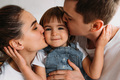 Portrait of a happy young family. Mom and dad kiss their baby - PhotoDune Item for Sale