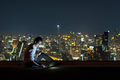 Asian businessman sitting and using the laptop over the cityscape background at night - PhotoDune Item for Sale