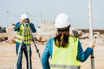 Selective focus of surveyors with digital level and survey ruler on construction site