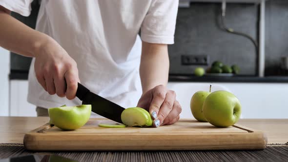 Girl Cutting Green Apple Into Slices on a Bamboo Board in Kitchen