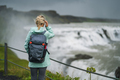 Blond woman with backpack and green jacket visit Gullfoss powerful famous waterfall in Iceland - PhotoDune Item for Sale