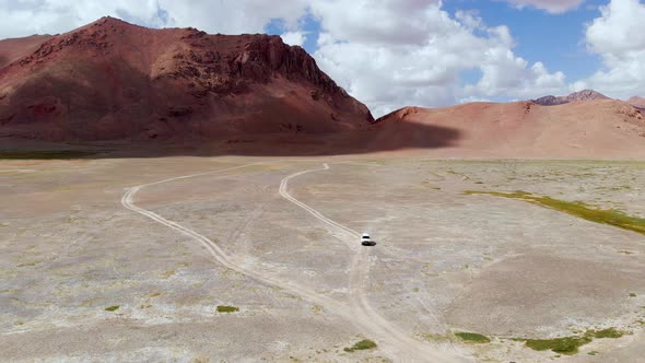 Aerial View of a Car Driving in a Curved Dirt Road in the Tajikistan Desert