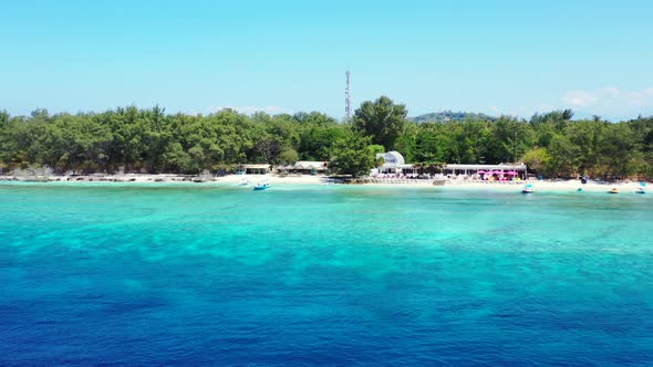 Beach bar surrounded by lush vegetation with boats floating on shallow blue turquoise lagoon on a su