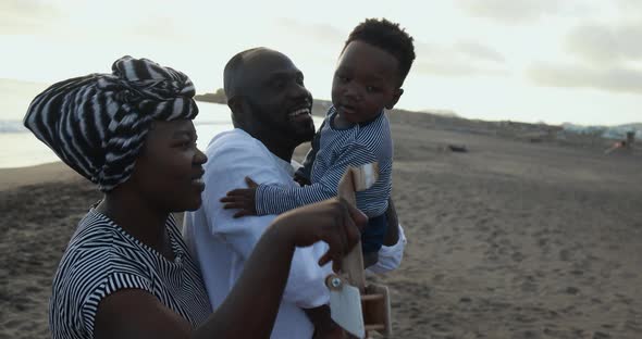 African parents and little son having fun with wood airplane on the beach