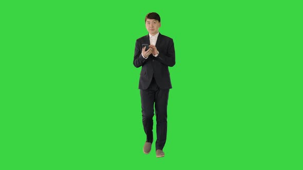 Asian Man in Suit Walks Using Mobile Phone on a Green Screen Chroma Key