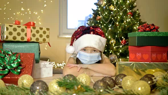 Sad Girl 67 Years Old Wearing a Santa Hat and a Protective Mask Sits Alone Against the Background of