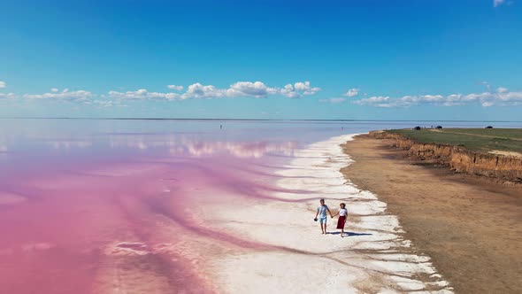 Aerial Footage of Lovely Couple Walking on Shore of Pink Mineral Lake
