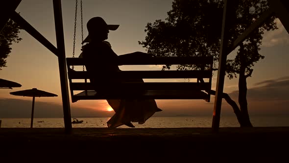 Elegant Woman on Water Front Swing During Sunset