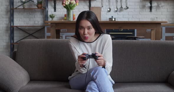 Portrait of Young Beautiful Asian Gamer Girl Sitting on Sofa and Playing in Video Games on Digital