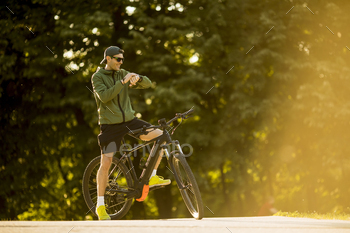 Young man with ebike, mountain bike with electric battery, checking time in the park