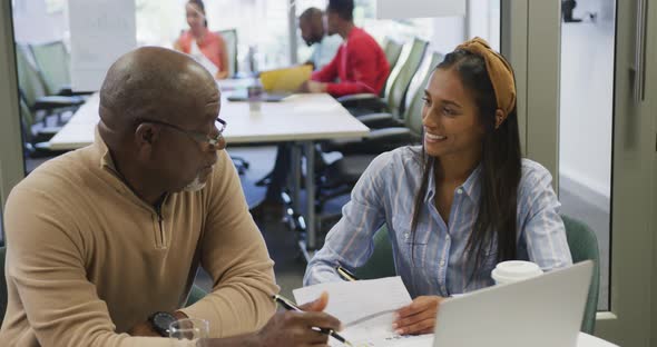 Diverse male and female business colleagues talking and holding documents in office