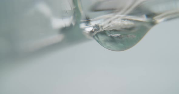 White transparent dripping slowly from a glass surface. Static macro shot.