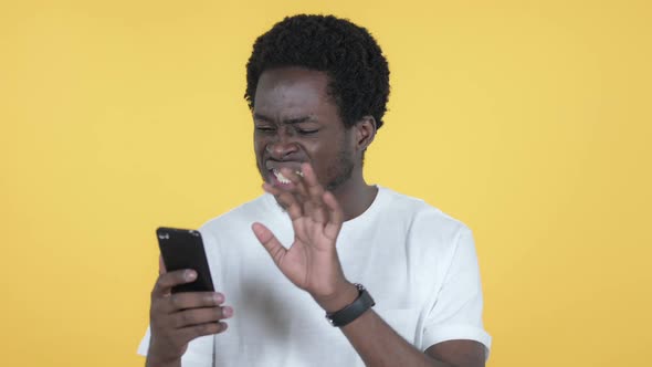 African Man Reacting to Loss on Smartphone Yellow Background