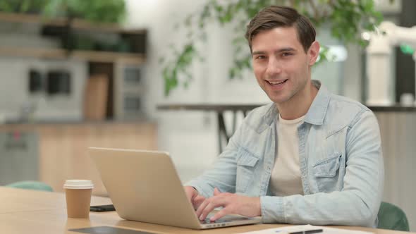 Creative Young Man with Laptop Smiling at Camera