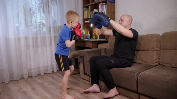 Father Boxing Coach Teaches His Son in Boxing Gloves to Hit Boxing Paws at Home